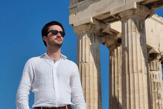 Man standing infront of greek temple. Photo.
