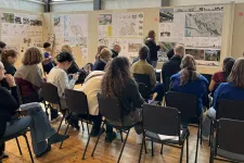 People in classroom following presentation in front of exhibition. Photo.