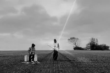 Two alienlike figures playing with a lightbeam. Photo.