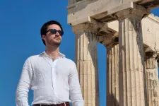 Man standing infront of greek temple. Photo.