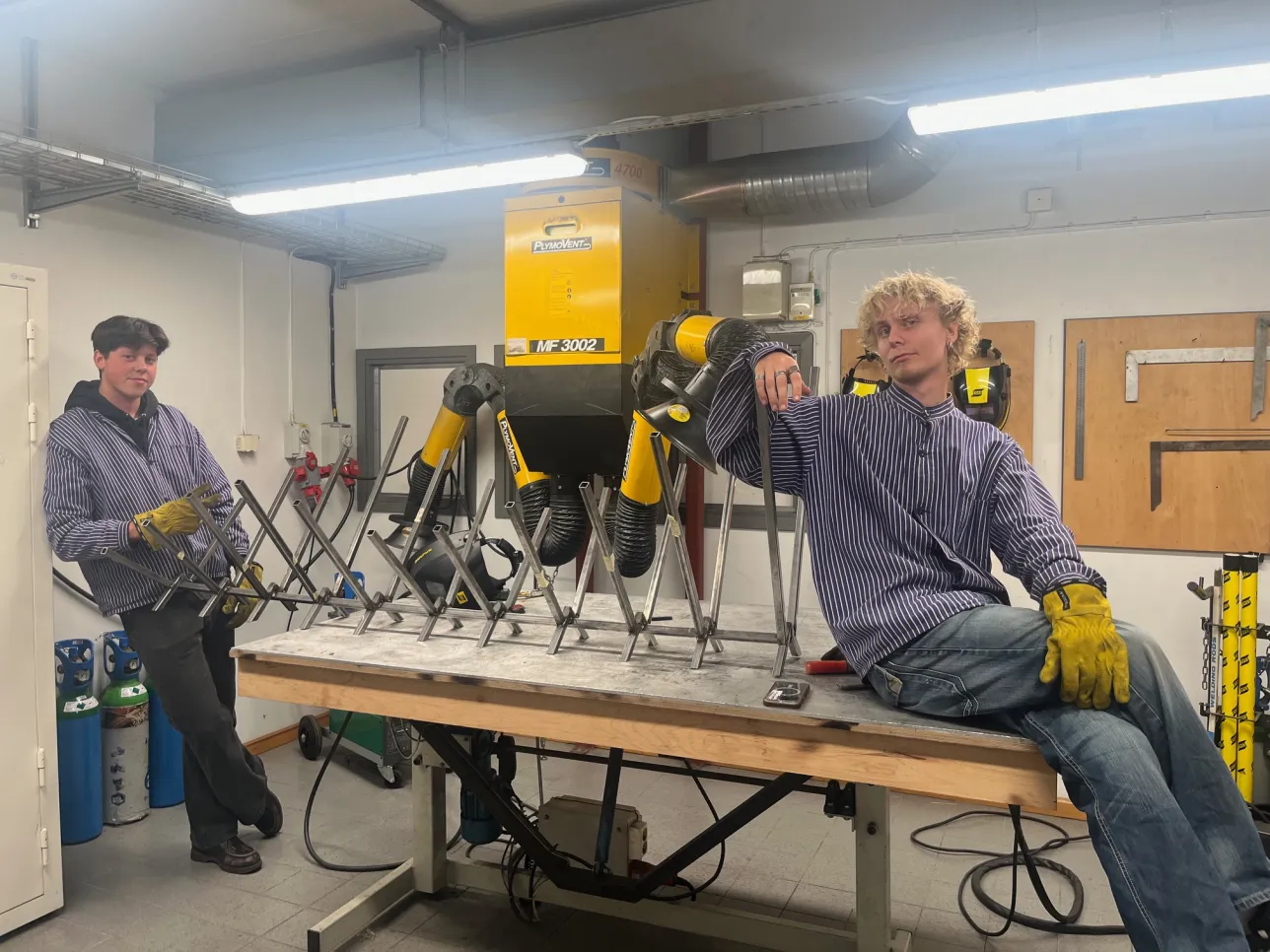 Two men sitting and standing next to metal chair, that they are building. Photo.
