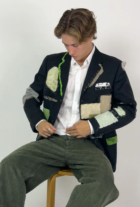 Man sitting on chair wearing a black suit jacket. Photo.