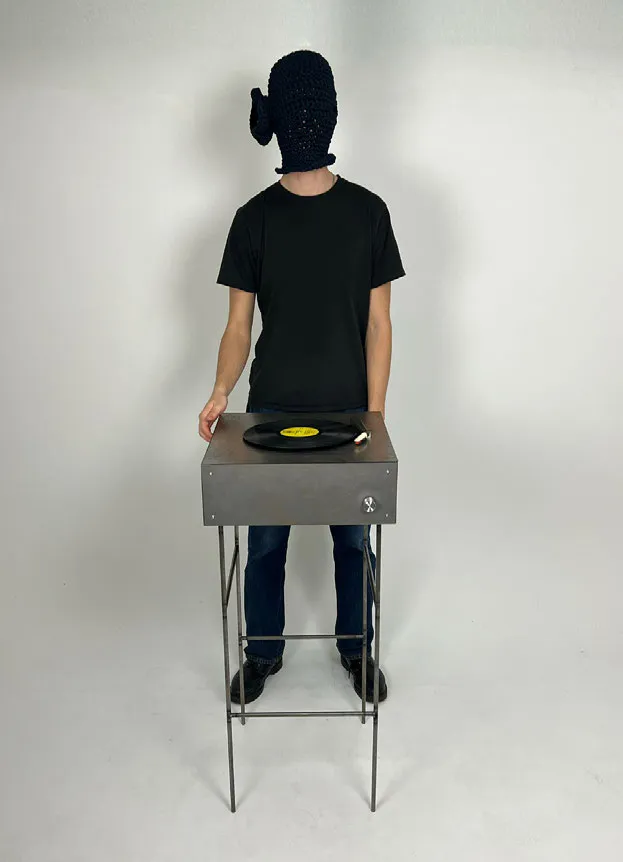 Man with covered face standing behind a vinyl player. Photo.