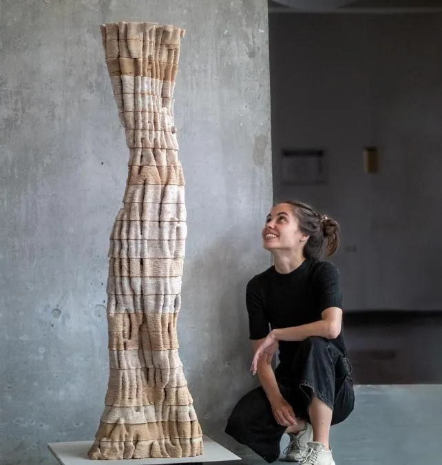 Female architect sits on the floor and looks up at the sculpture they created for the project. Photo.
